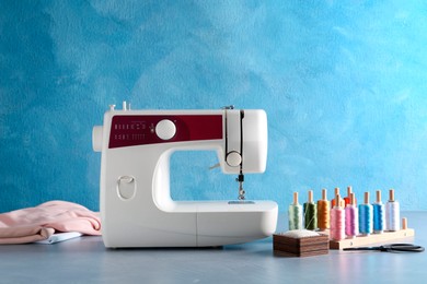 Photo of White sewing machine and craft accessories on gray table near light blue wall