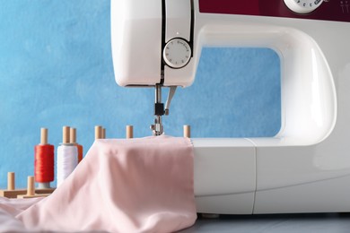 White sewing machine with color fabric on table against light blue background, closeup