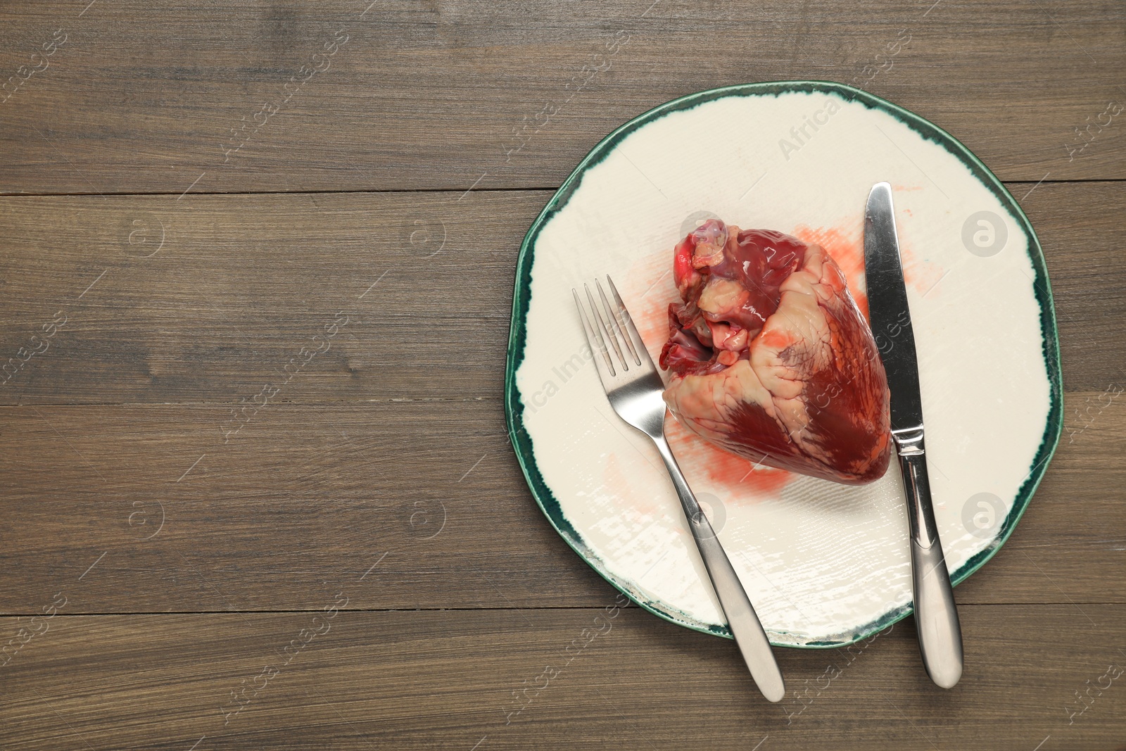 Photo of Raw heart, fork and knife on wooden table, top view. Space for text