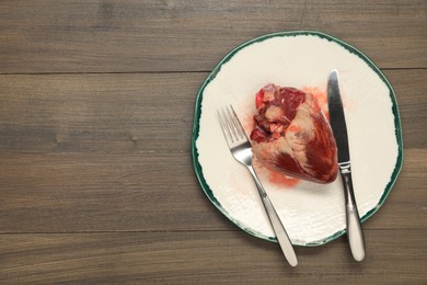 Raw heart, fork and knife on wooden table, top view. Space for text