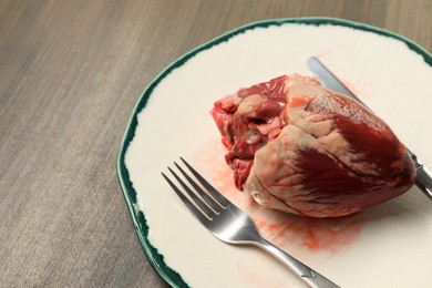 Raw heart, fork and knife on wooden table. Space for text