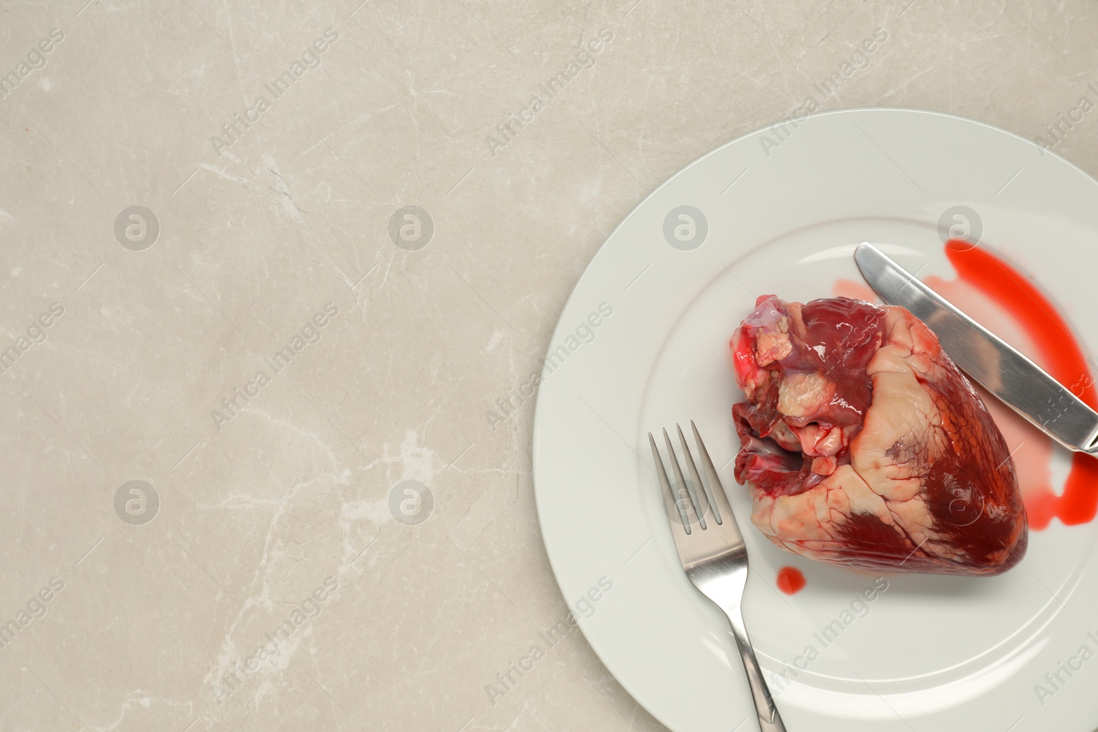 Photo of Raw heart, fork and knife on light grey marble table, top view. Space for text