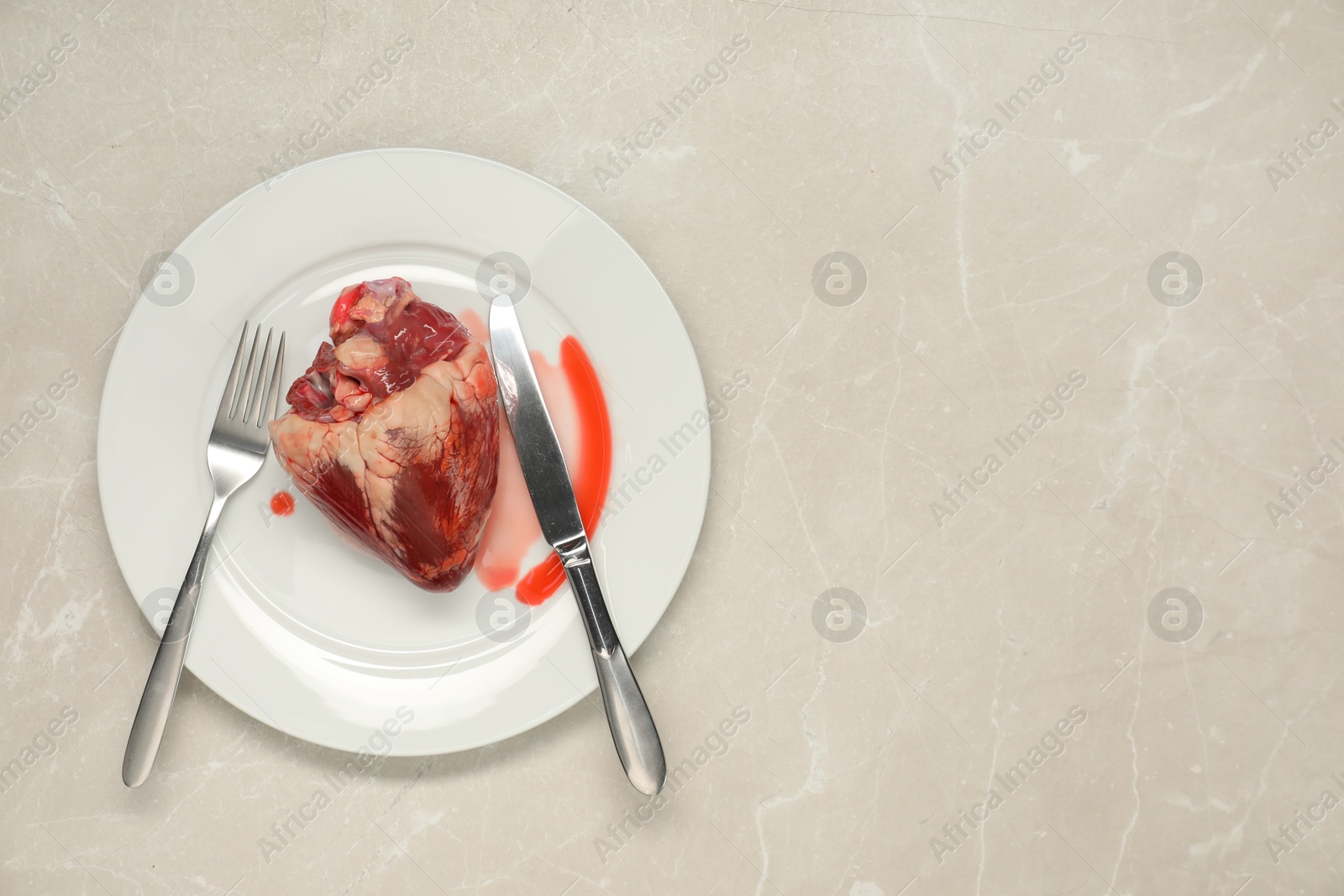 Photo of Raw heart, fork and knife on light grey marble table, top view. Space for text