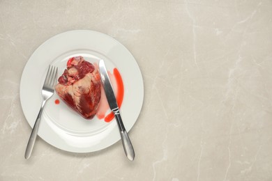 Raw heart, fork and knife on light grey marble table, top view. Space for text