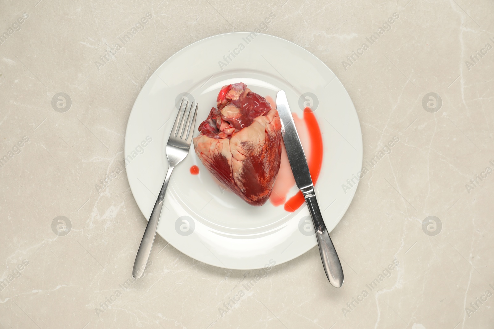 Photo of Raw heart, fork and knife on light grey marble table, top view