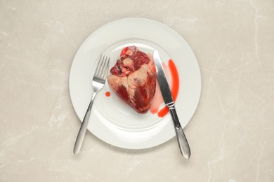 Photo of Raw heart, fork and knife on light grey marble table, top view