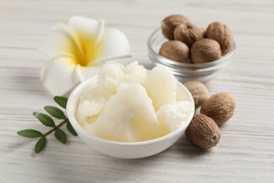 Natural shea butter in bowl, nuts, green twig and plumeria flower on wooden table