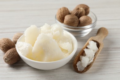 Natural shea butter in bowl and nuts on wooden table, closeup