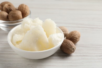 Natural shea butter in bowl and nuts on wooden table, closeup