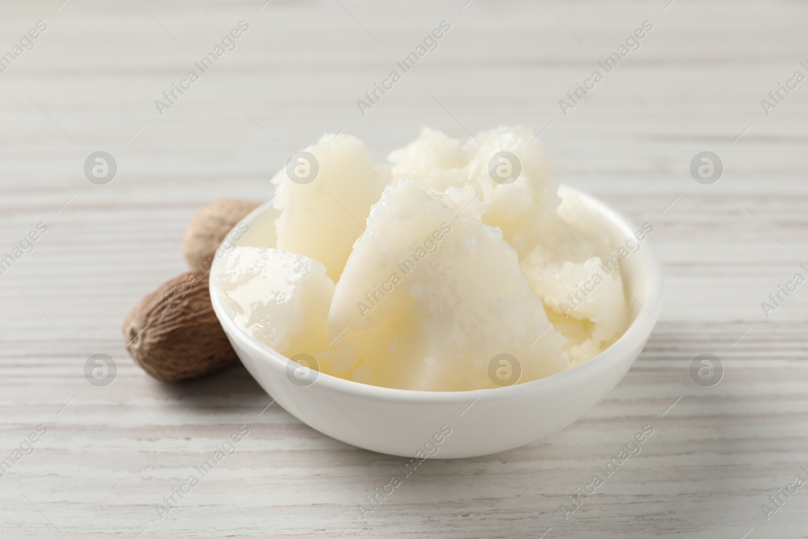 Photo of Natural shea butter in bowl and nuts on wooden table, closeup