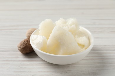 Natural shea butter in bowl and nuts on wooden table, closeup