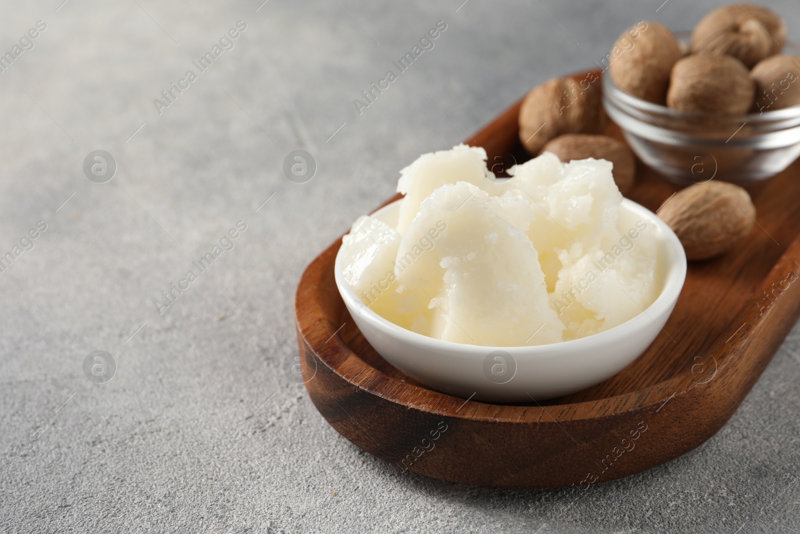 Photo of Natural shea butter in bowl and nuts on grey table, space for text