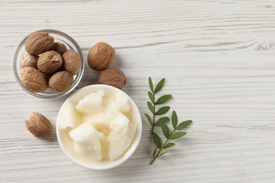 Natural shea butter in bowl, nuts and green leaves on wooden table, top view. Space for text