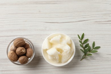 Natural shea butter in bowl, nuts and green leaves on wooden table, top view. Space for text