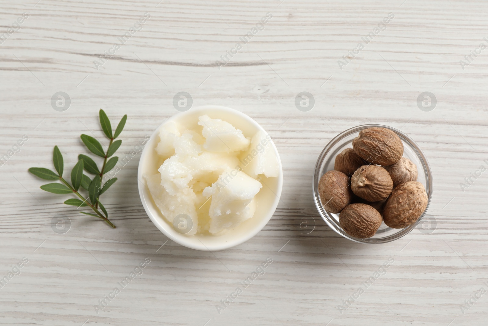 Photo of Natural shea butter in bowl, nuts and green leaves on wooden table, top view