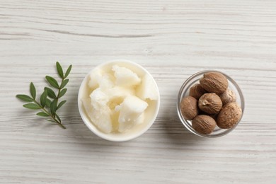 Natural shea butter in bowl, nuts and green leaves on wooden table, top view