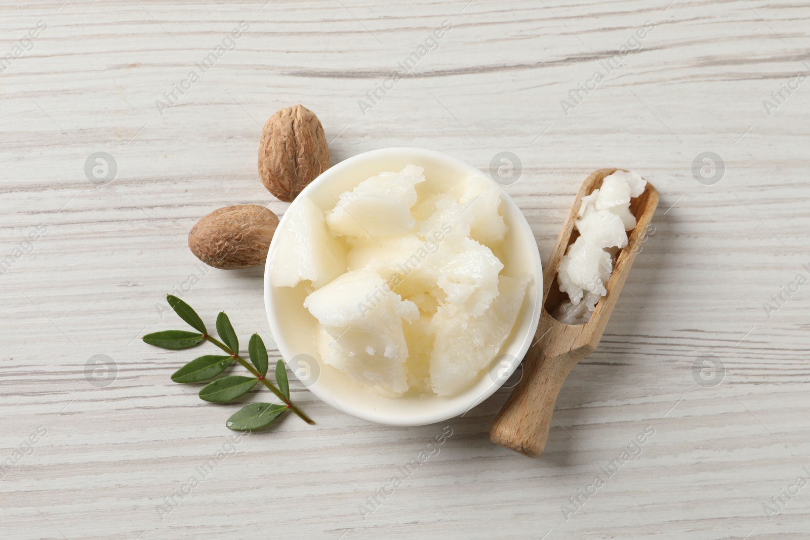 Photo of Natural shea butter in bowl, nuts and green twig on wooden table, top view