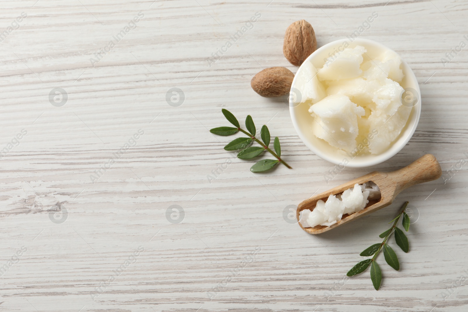 Photo of Natural shea butter in bowl, nuts and green leaves on wooden table, top view. Space for text