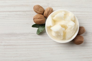 Natural shea butter in bowl, nuts and green leaves on wooden table, top view. Space for text