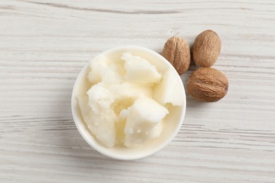 Photo of Natural shea butter in bowl and nuts on wooden table, top view