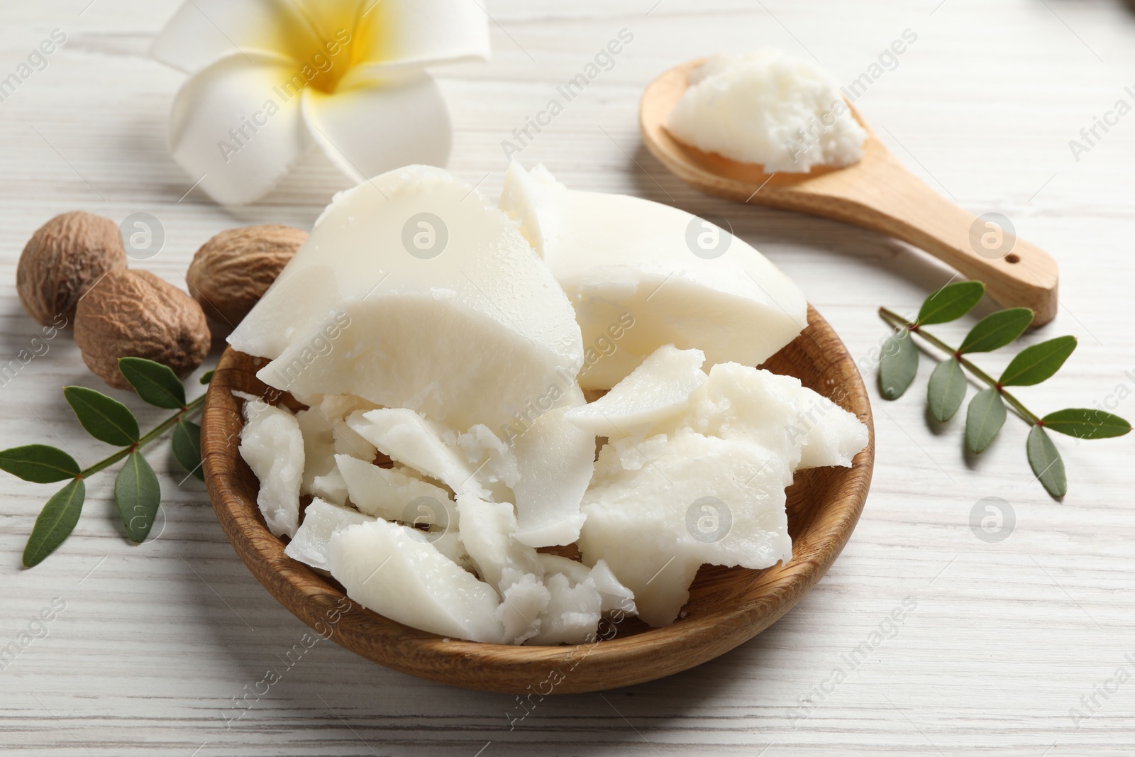 Photo of Natural shea butter, nuts, plumeria flower and green leaves on wooden table