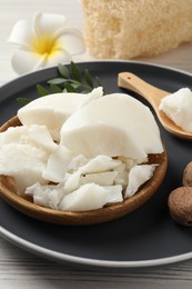 Photo of Natural shea butter, nuts, plumeria flower and loofah sponge on wooden table