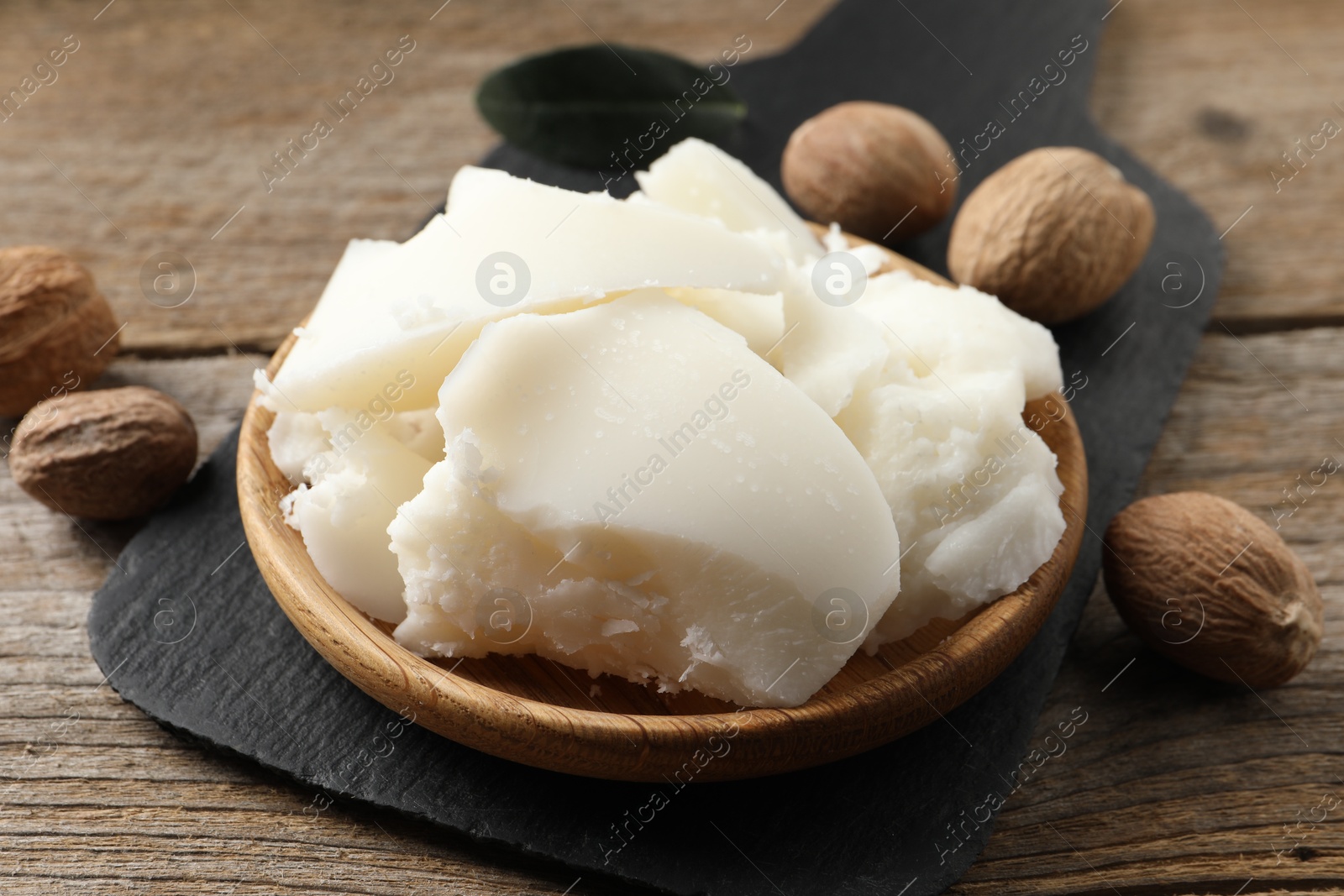 Photo of Natural shea butter and nuts on wooden table, closeup