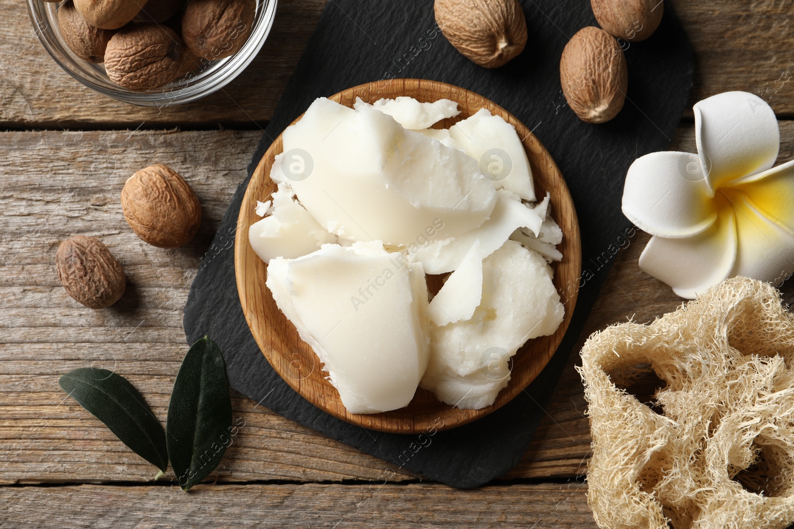 Photo of Natural shea butter, nuts, plumeria flower and loofah sponge on wooden table, top view