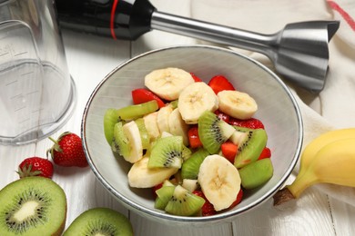 Photo of Hand blender kit, fresh fruits and strawberries in bowl on white wooden table, closeup