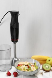 Photo of Hand blender kit, fresh fruits and strawberries in bowl on white wooden table