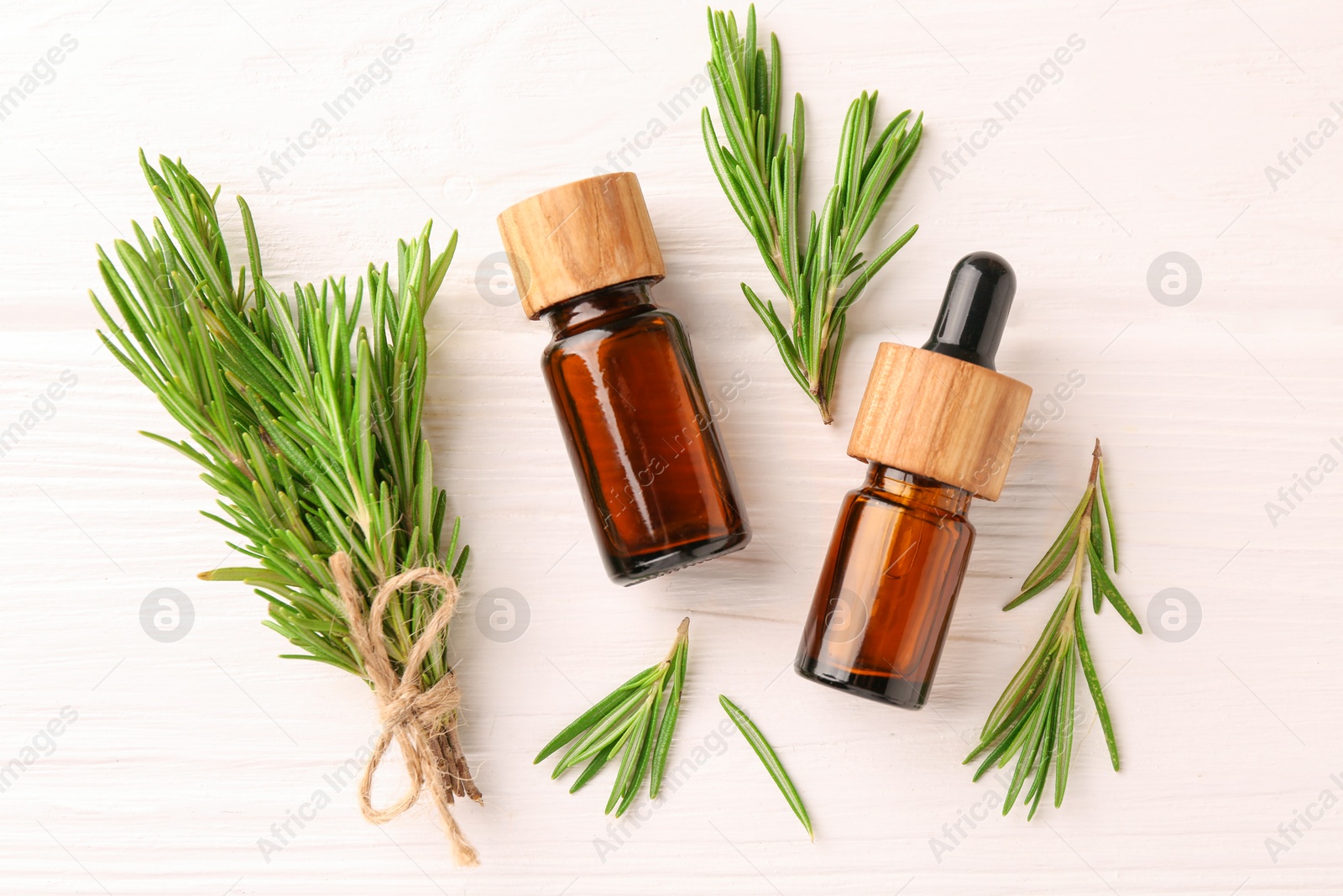 Photo of Essential oil in bottles and rosemary on white wooden table, flat lay