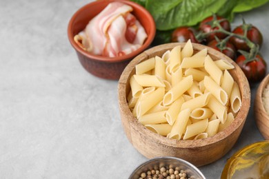 Photo of Raw pasta, bacon and fresh ingredients on light grey table, space for text