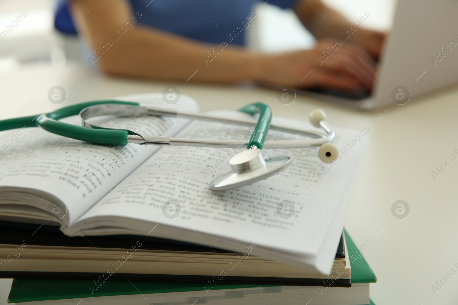 Photo of Doctor at white table in hospital, focus on medical stethoscope and books