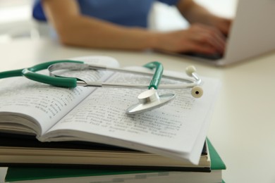 Photo of Doctor at white table in hospital, focus on medical stethoscope and books