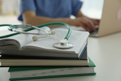 Photo of Doctor at white table in hospital, focus on medical stethoscope and books