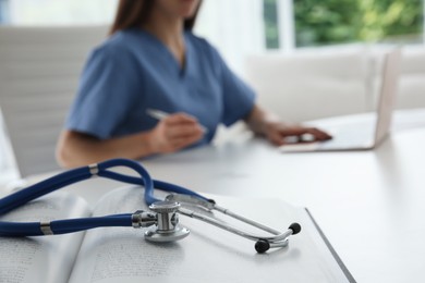 Photo of Doctor at white table in hospital, focus on medical stethoscope and book