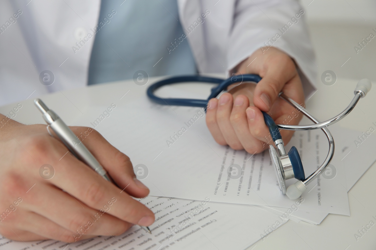 Photo of Doctor with stethoscope at white table in hospital, closeup