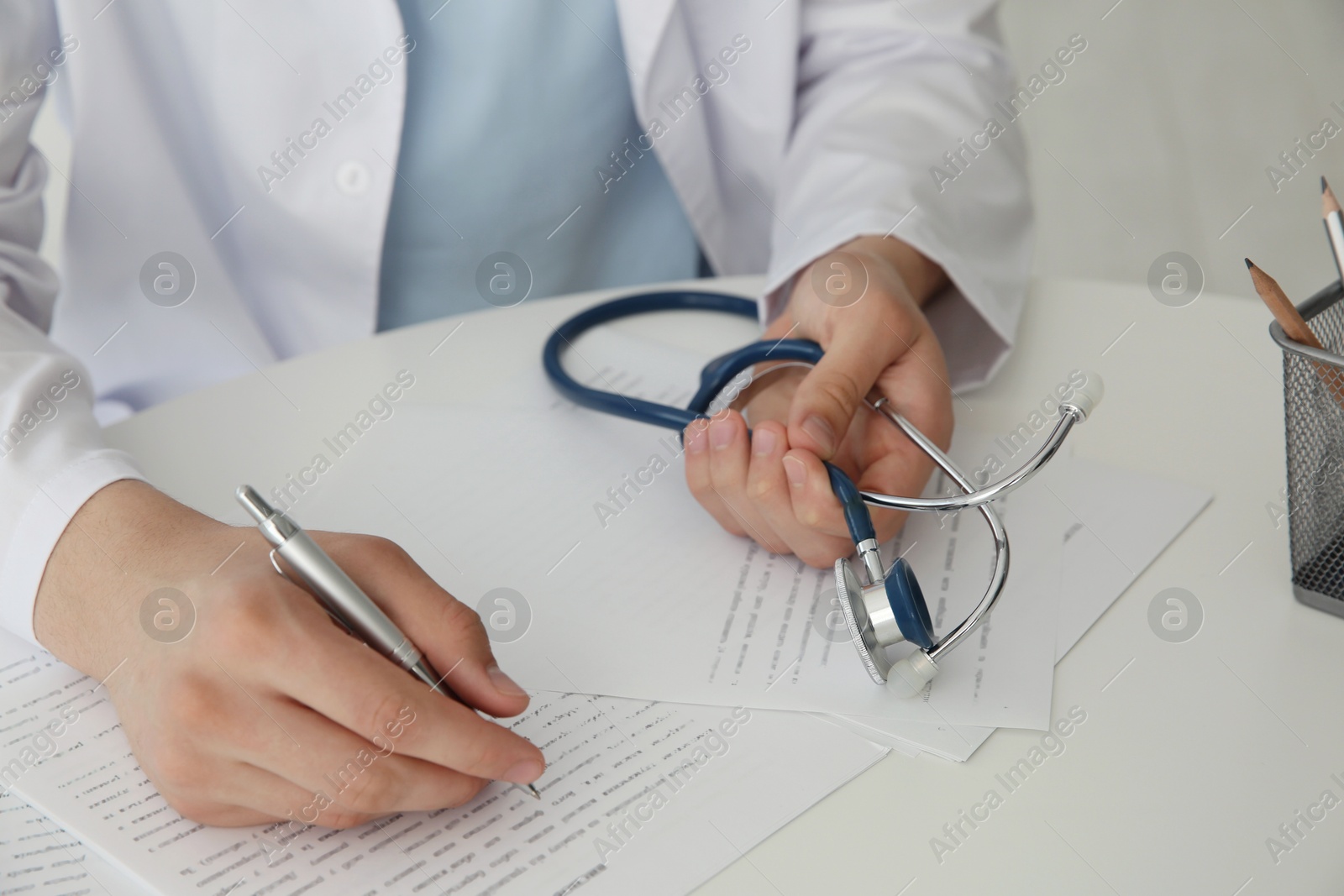 Photo of Doctor with stethoscope at white table in hospital, closeup