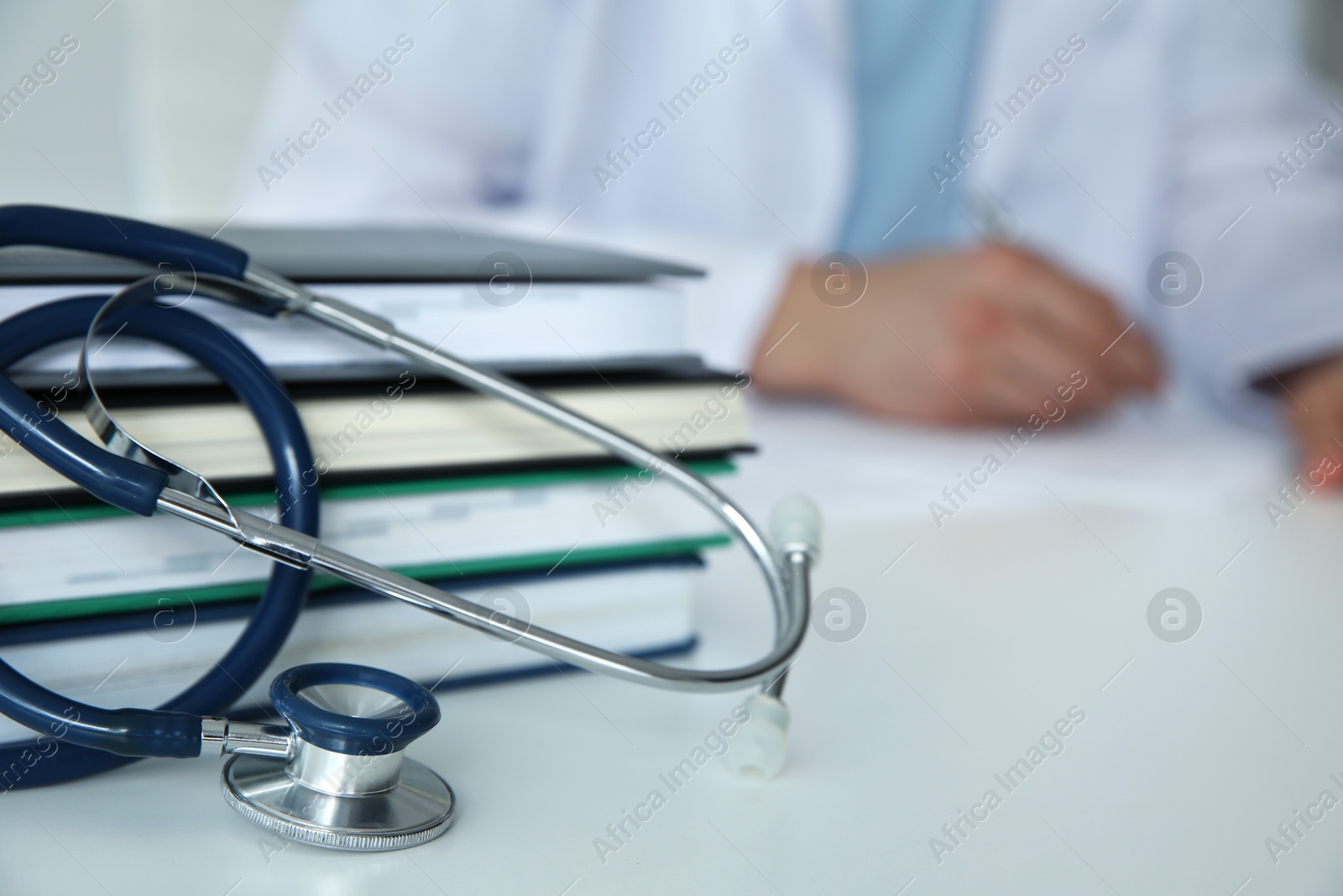 Photo of Doctor at white table in hospital, focus on medical stethoscope and books