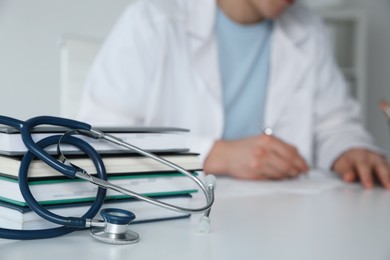 Photo of Doctor at white table in hospital, focus on medical stethoscope and books