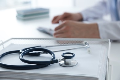 Photo of Doctor at white table in hospital, focus on medical stethoscope