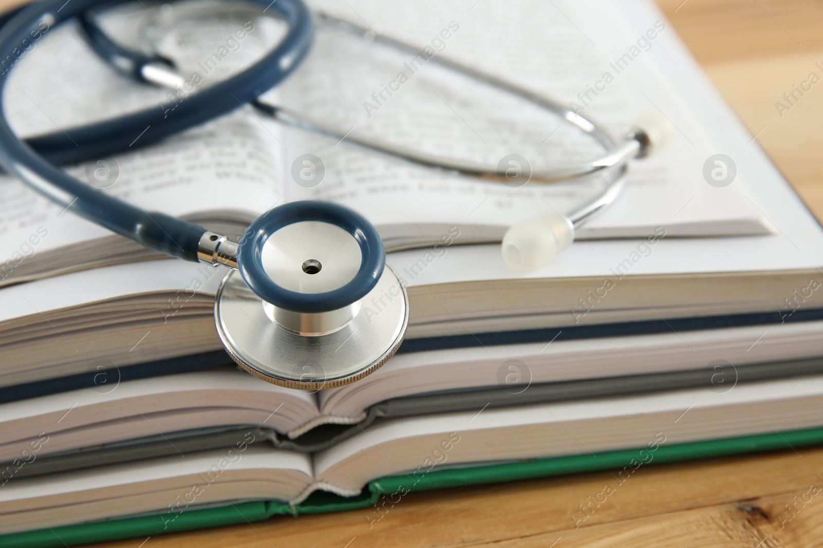 Photo of One new medical stethoscope and books on wooden table, closeup