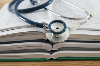 Photo of One new medical stethoscope and books on wooden table, closeup