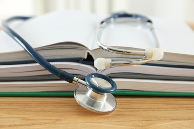 Photo of One new medical stethoscope and books on wooden table, closeup