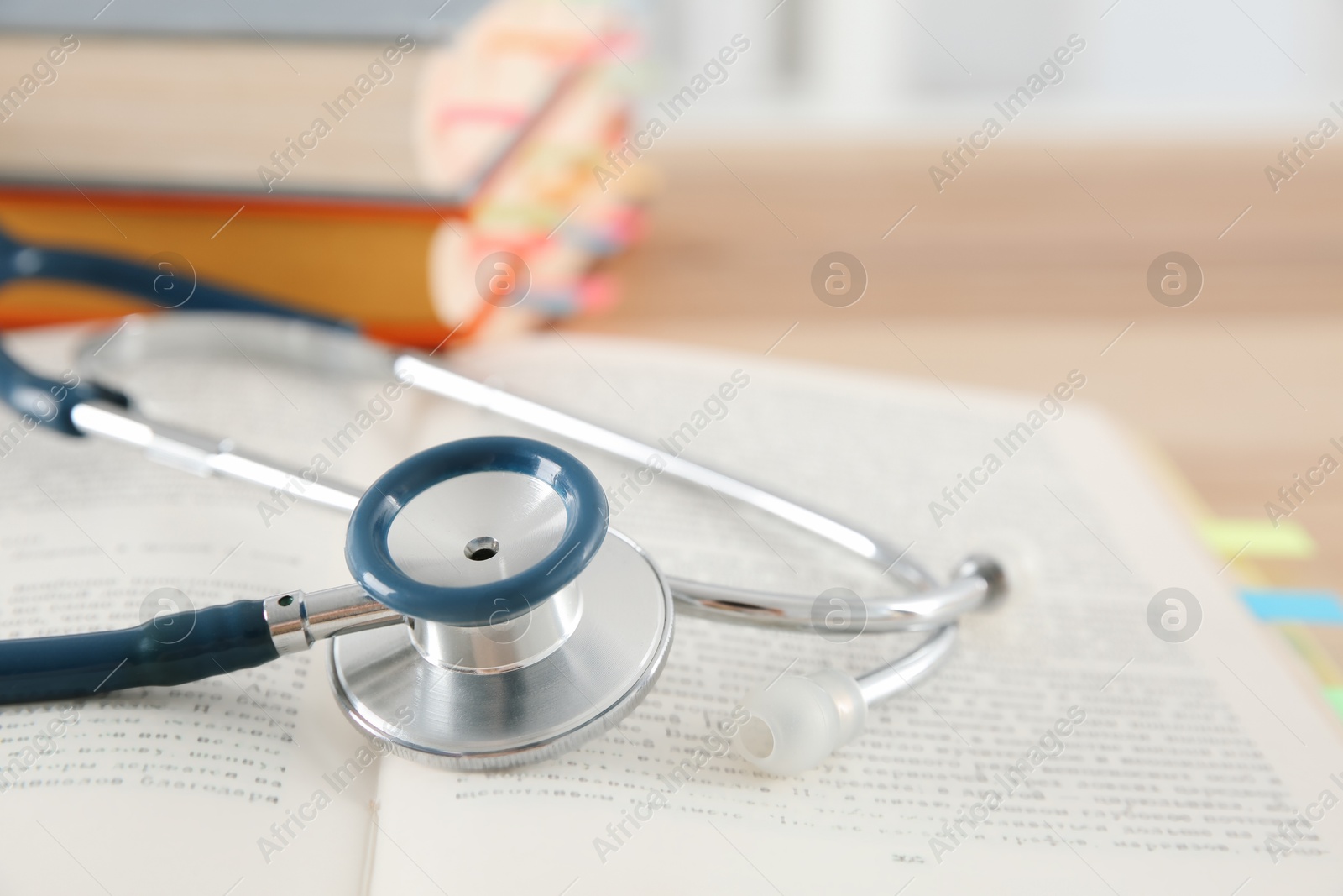 Photo of One new medical stethoscope and books on wooden table, closeup