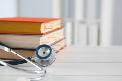 Photo of One new medical stethoscope and books on wooden table, closeup. Space for text