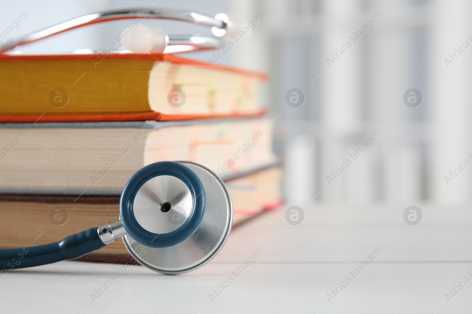 Photo of One new medical stethoscope and books on white table, closeup. Space for text