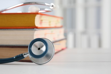 Photo of One new medical stethoscope and books on white table, closeup. Space for text