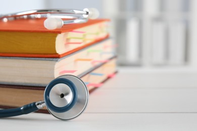 Photo of One new medical stethoscope and books on white table, closeup. Space for text