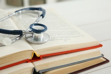 Photo of One new medical stethoscope and books on white wooden table, closeup